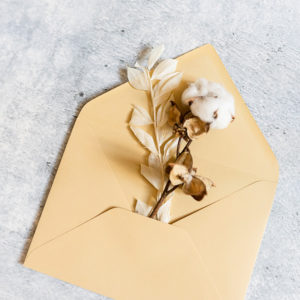 Schräge Aufsicht von oben:geöffneter Briefumschlag mit Trockenblumen und Accessoires
